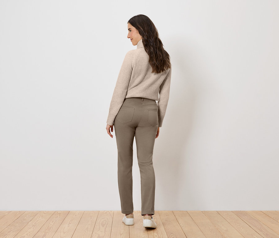 Frau mit beigem Pullover und braunen Hosen, die mit dem Rücken zum Betrachter steht.