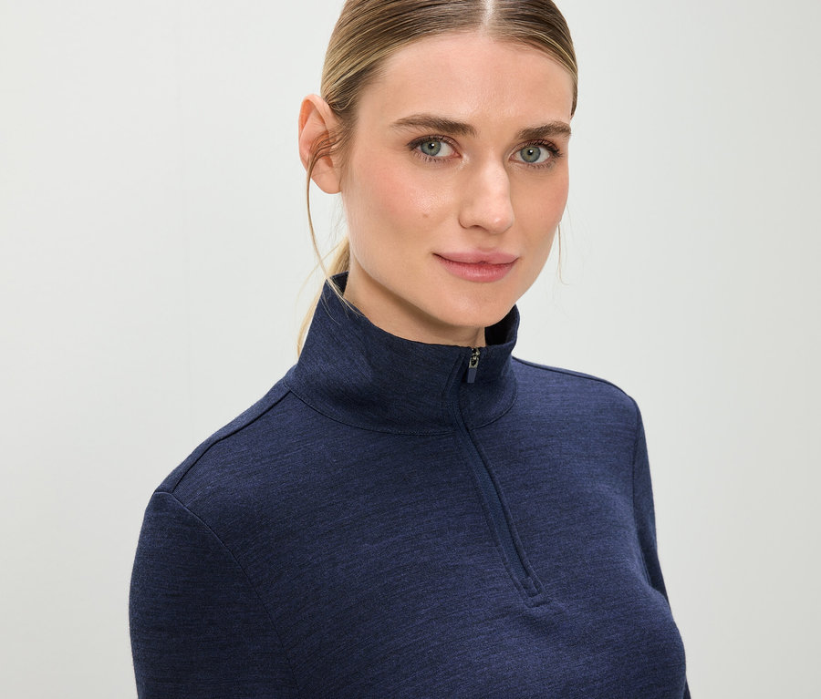 Porträt einer blonden Frau in einem blauen Langarmshirt mit Reißverschluss.