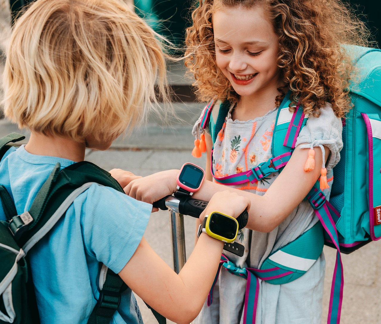 Zwei Kinder liegen in einem grünen Zelt auf einer Wiese. Der Junge links trägt eine braune Kappe und eine Uhr am Handgelenk. Das Mädchen rechts hat lockiges Haar. Der Junge trägt eine Kids Watch Xplora X6Play