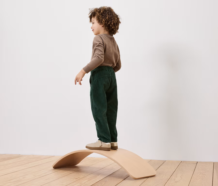 Ein Junge mit lockigem Haar steht auf einem hölzernen Balance Board.