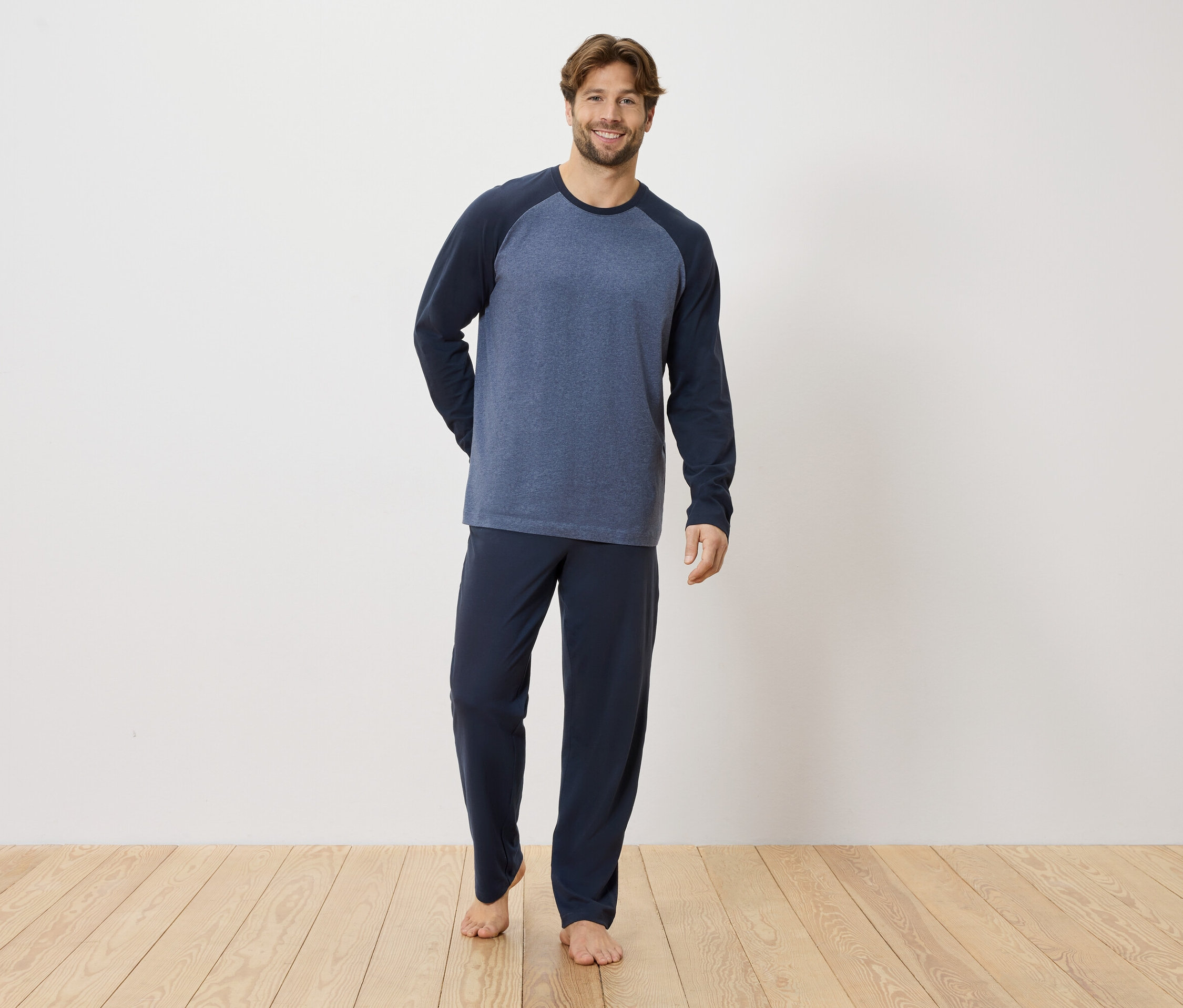 Mann steht barfuß auf Holzboden und trägt einen dunkelblauen Schlafanzug.
