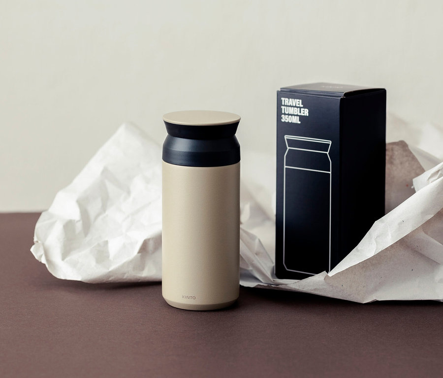 Ein beiger Kinto Reisebecher steht neben seiner schwarzen Verpackung.