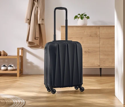 Schwarzer Rollkoffer mit ausziehbarem Griff steht auf einem hellen Holzboden.