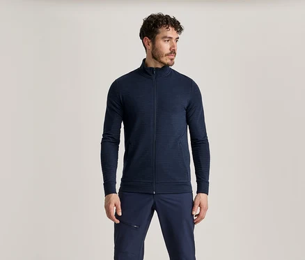 Mann mit dunklen, lockigen Haaren, Bart und Schnurrbart, trägt eine marineblaue Jacke mit Reißverschluss und marineblaue Hose.