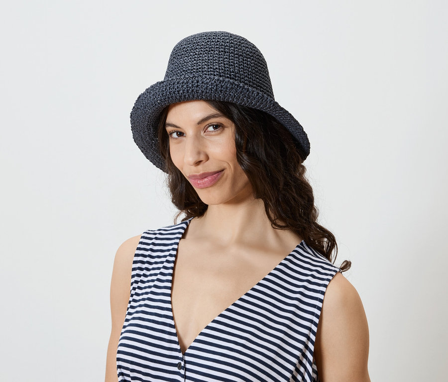 Frau mit dunklen, gewellten Haaren trägt einen marineblauen Häkelhut und ein gestreiftes Tanktop.