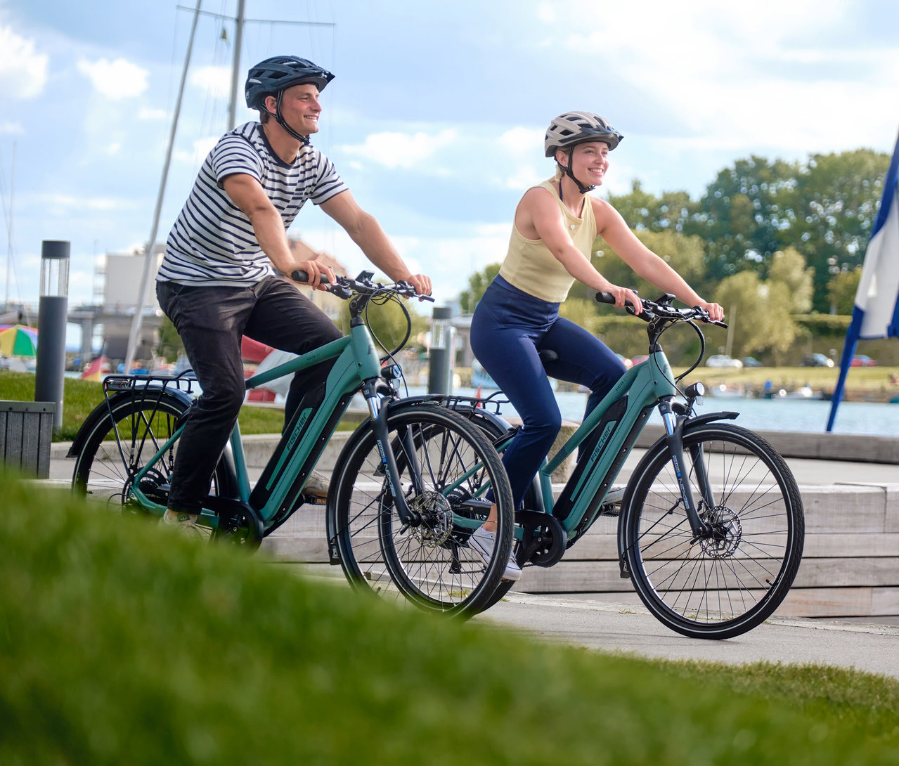 Ein Mann und eine Frau fahren je ein grünes FISCHER Trekking E-Bike VIATOR 2.1 ACTIVE mit Diamant-Rahmen auf einem Uferweg.