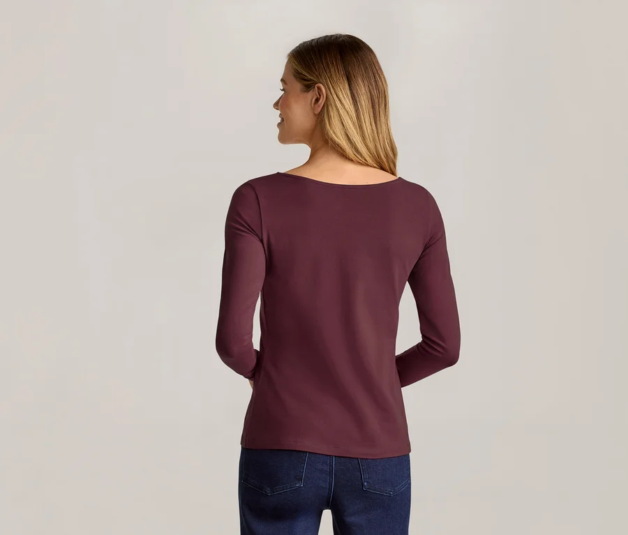 Frau von hinten, trägt ein weinrotes Langarmshirt und Jeans vor einem hellgrauen Hintergrund.