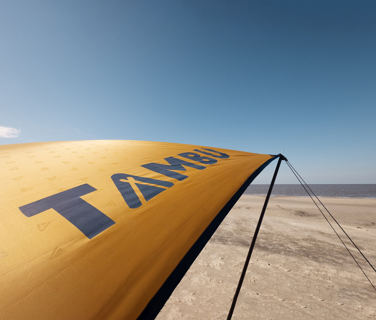 Nahaufnahme eines Tambu »CHADA« Tarp/Sonnensegels am Strand unter blauem Himmel.