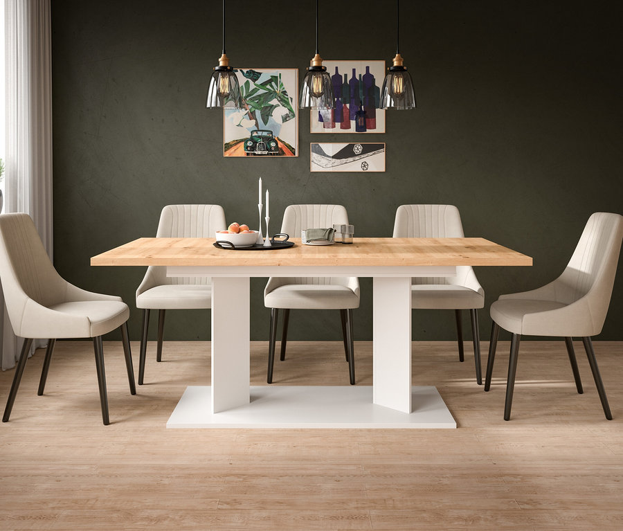 Modernes Esszimmer mit rechteckigem Tisch aus hellem Holz auf weißem Sockel, umgeben von sechs beigefarbenen Polsterstühlen. Drei Glaspendelleuchten hängen über dem Tisch, auf dem eine Obstschale und Kerzen stehen. Drei Kunstwerke schmücken die dunkelgrüne Wand.