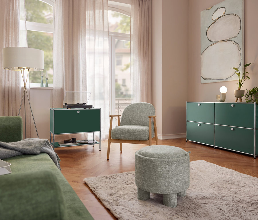 Wohnzimmer mit grünem Sofa, einer Eglo Stehleuchte »Fondachelli«, einem Sideboard Metall »CN3« mit 1 Klappenfach und Plattenspieler. Ein Sessel mit Holzgestell und ein Sitzpouf stehen auf einem Teppich. Rechts ein Sideboard Metall »CN3« mit 4 Klappenfächern und einer Trio Keramik-Tischleuchte.
