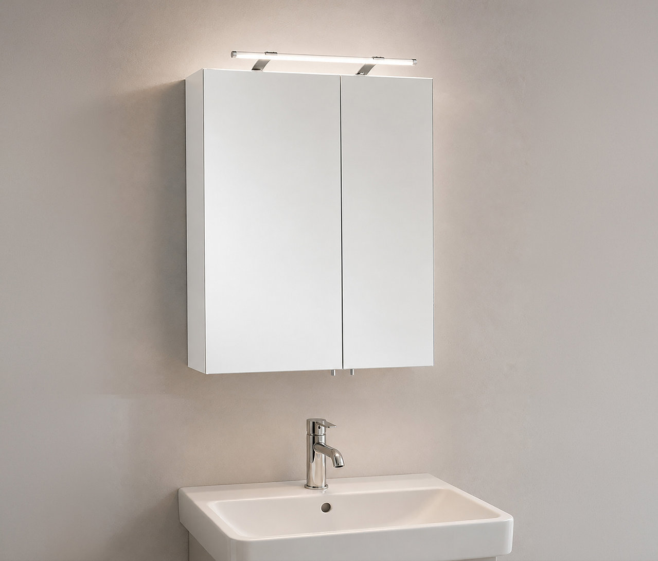 Weißer Spiegelschrank »Dorina« mit zwei Spiegeltüren und Lichtleiste darüber, über einem weißen Waschbecken mit Chromarmatur an einer hellen Wand.