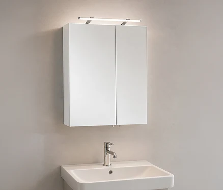 Weißer Spiegelschrank »Dorina« mit zwei Spiegeltüren und Lichtleiste darüber, über einem weißen Waschbecken mit Chromarmatur an einer hellen Wand.