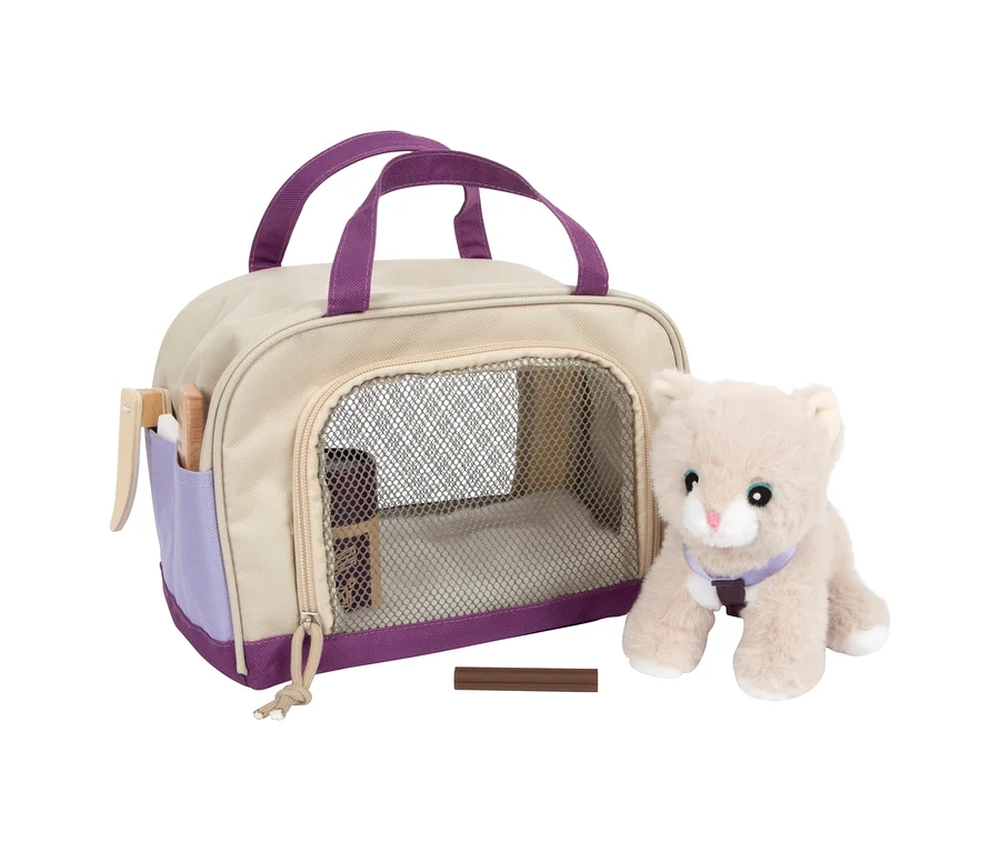 Eine beigefarbene small foot Plüschkatze mit lila Geschirr steht neben einer beigen Tragetasche mit lila Akzenten und Netzfenster. In der Tasche befinden sich Pflegeutensilien und ein brauner Spielzeugknochen liegt davor.