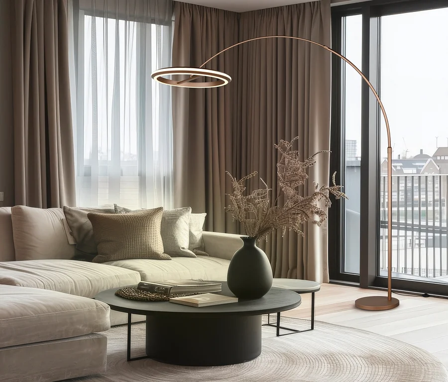 Modernes Wohnzimmer mit hellem Ecksofa, rundem Couchtisch mit Vase und Büchern, und einem runden Teppich. Eine gebogene Stehlampe mit kreisförmigem LED-Licht steht daneben.