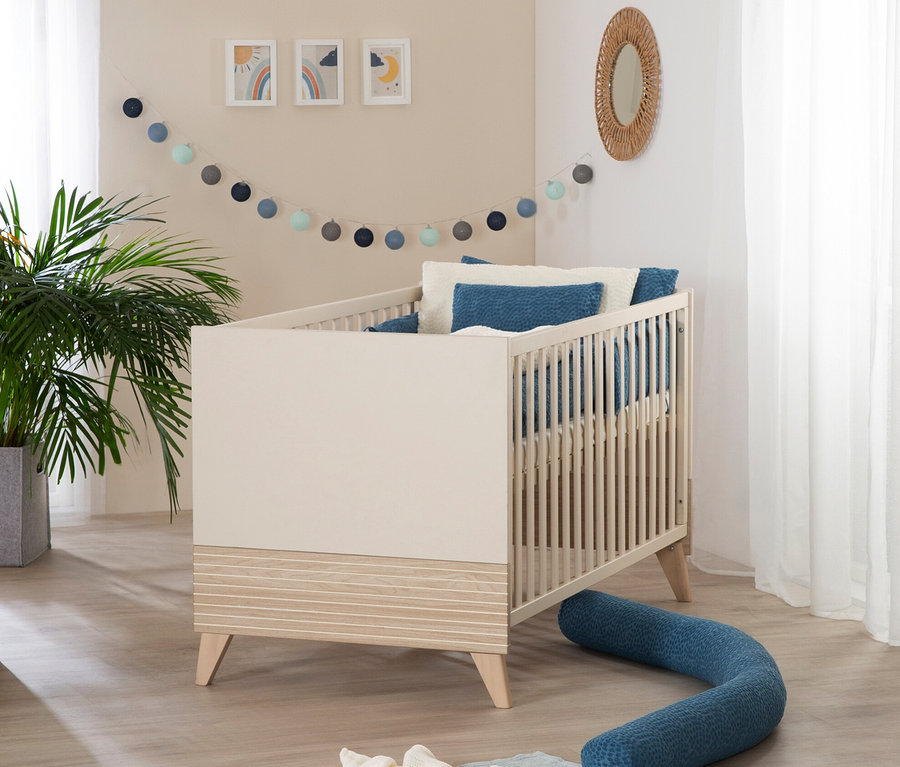 Ein roba Set »Sidney« 3-teilig, Kaschmir Kinderbett mit blauen Kissen und Nestchen steht in einem Zimmer mit einer Pflanze und Dekorationen.