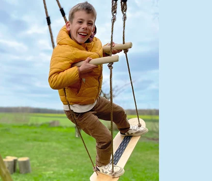 Ein Junge in gelber Jacke lacht und spielt auf einer small foot Skateboard-Schaukel.