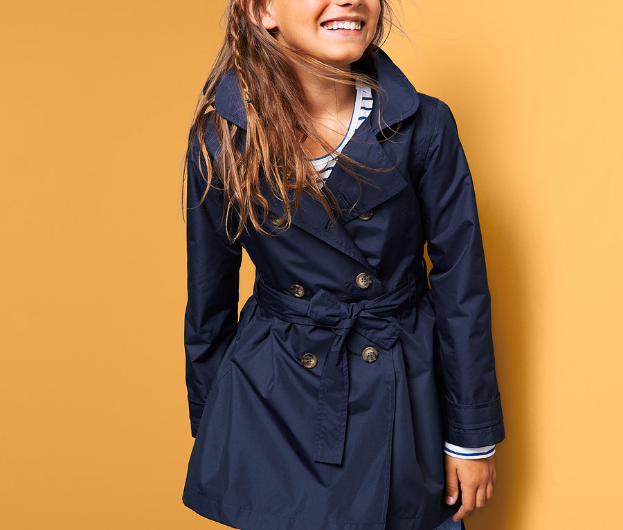Lächelndes Mädchen trägt einen dunkelblauen Allwetter-Trenchcoat.