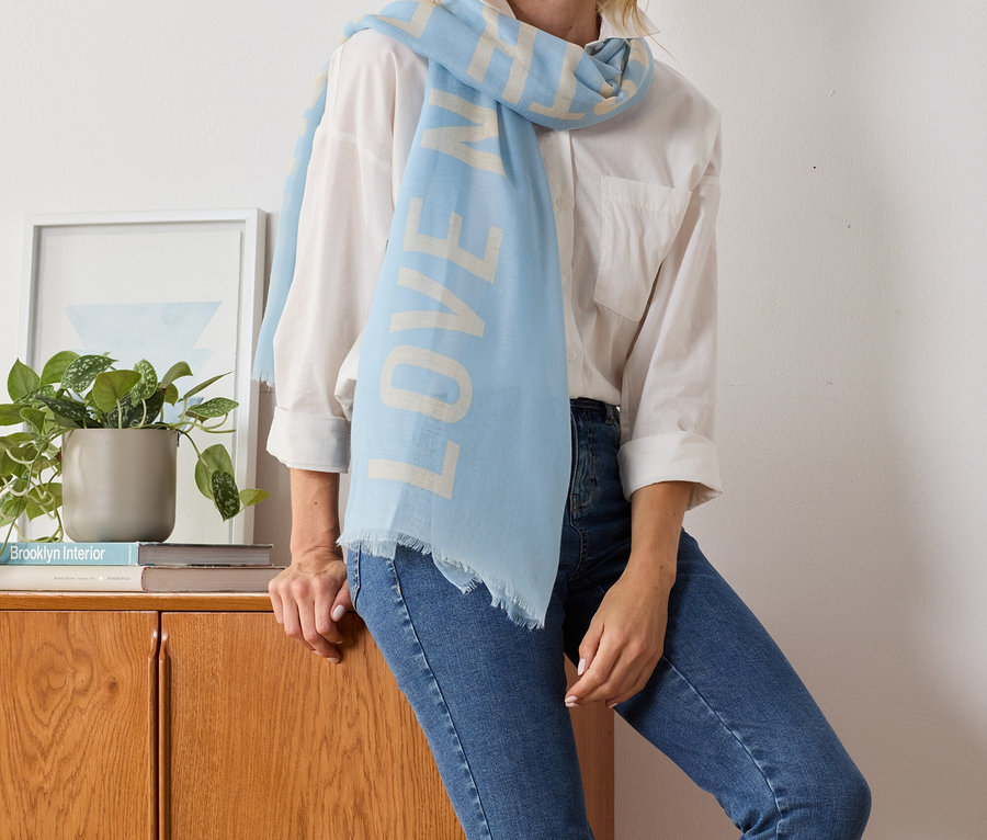 Blonde Frau posiert mit hellblauem Webschal mit Statement-Print.