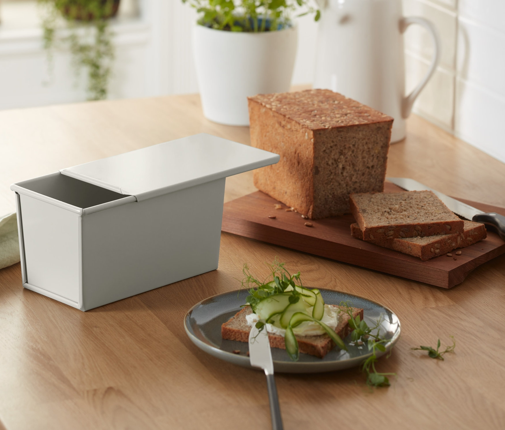 Vollkorn- und Toastbrot-Backform und gebackenes Brot liegen auf einem Holztisch.