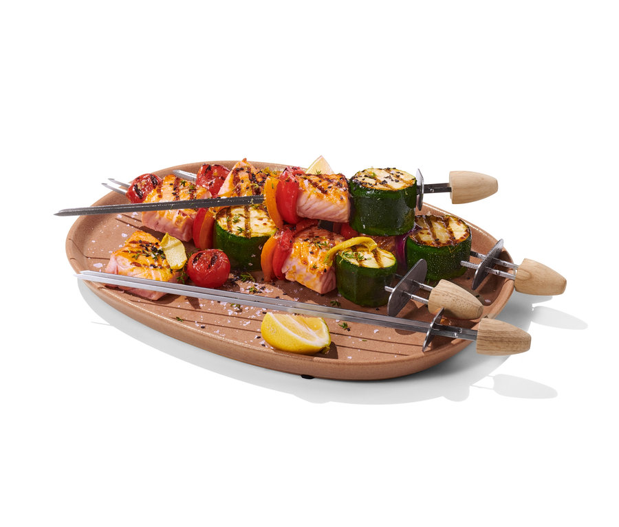 Vier Schaschlikspieße mit Lachs, Zucchini, Paprika und Tomaten auf einem braunen Teller.