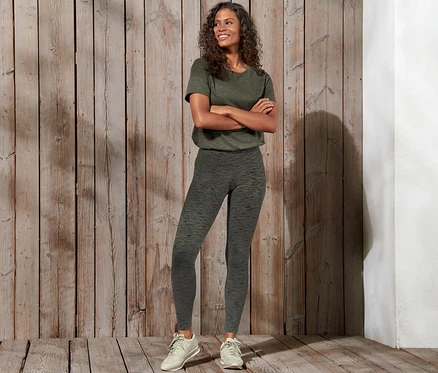 Lächelnde Frau posiert mit verschränkten Armen und trägt eine Sporttight.