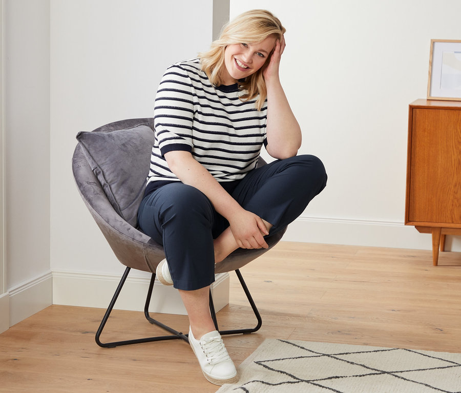 Frau sitzt im Sessel, trägt Feinstrickpullover mit Halbarm, Cropped Bengalin-Hose und Canvas-Sneaker.