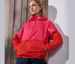 Eine Frau, die sich an eine Wand lehnt, trägt einen Windbreaker und eine dunkelblaue Hose.