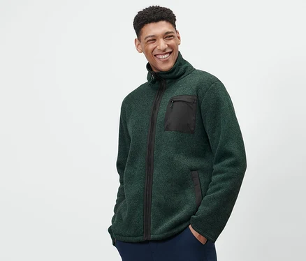 Ein Mann trägt eine grüne Thermo-Strickfleecejacke und dunkelblaue Hosen.