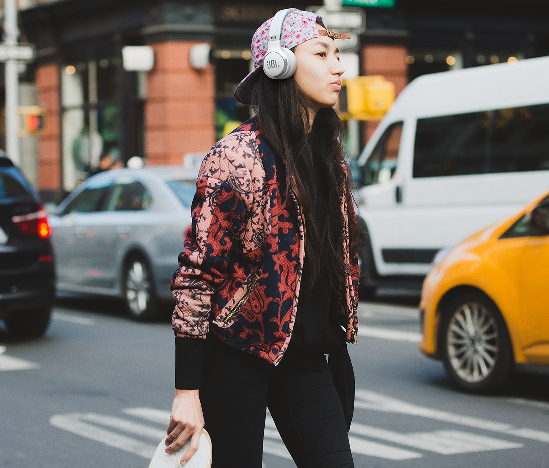 Junge Frau überquert die Straße und trägt weiße JBL »Live 670 NC« On-Ear-Kopfhörer.