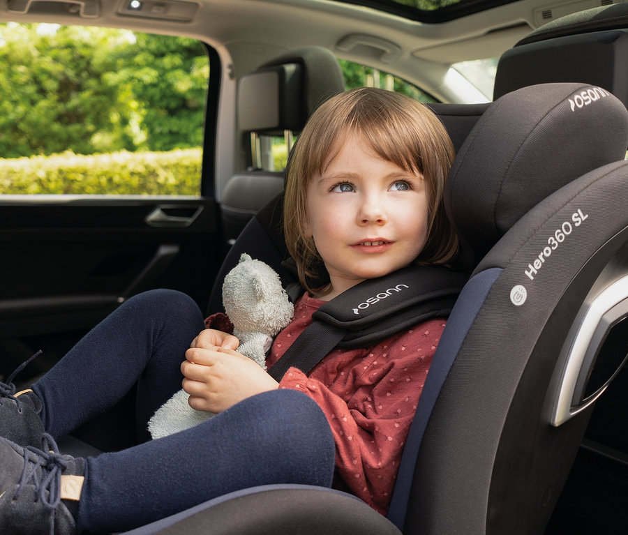 Mädchen sitzt im Osann Kindersitz »Hero360 SL« und hält einen Teddybären.
