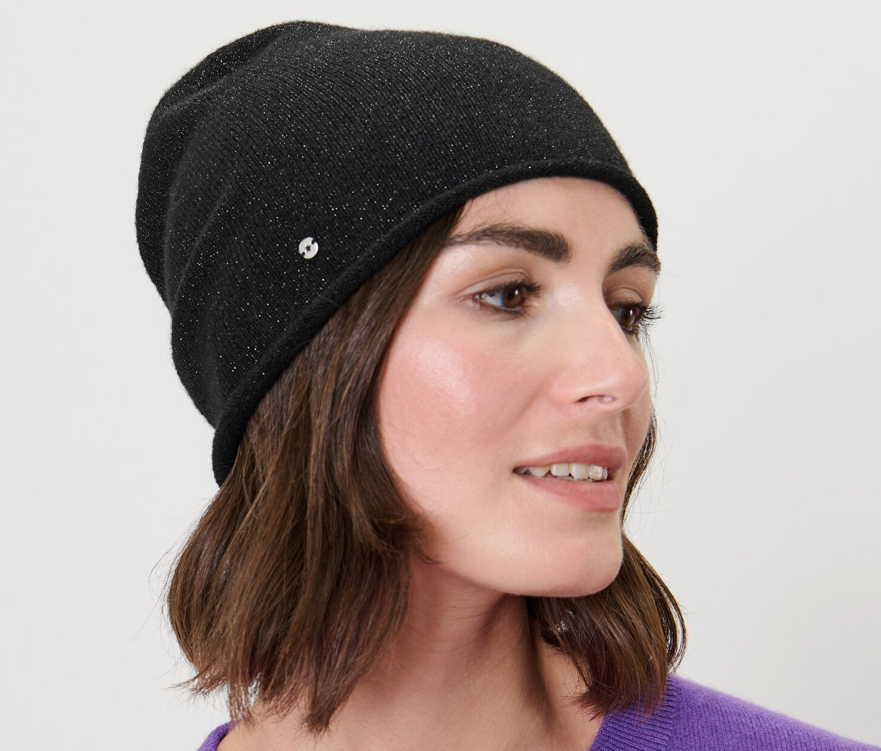 Frau mit braunen Haaren trägt eine glitzernde Feinstrick-Beanie in Schwarz.