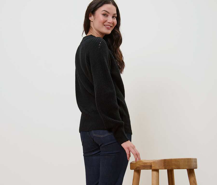 Frau lächelt über die Schulter und posiert in schwarzem Strickpullover.