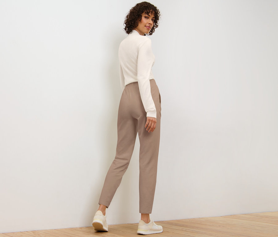 Frau blickt über die Schulter und trägt eine beige Joggpants.