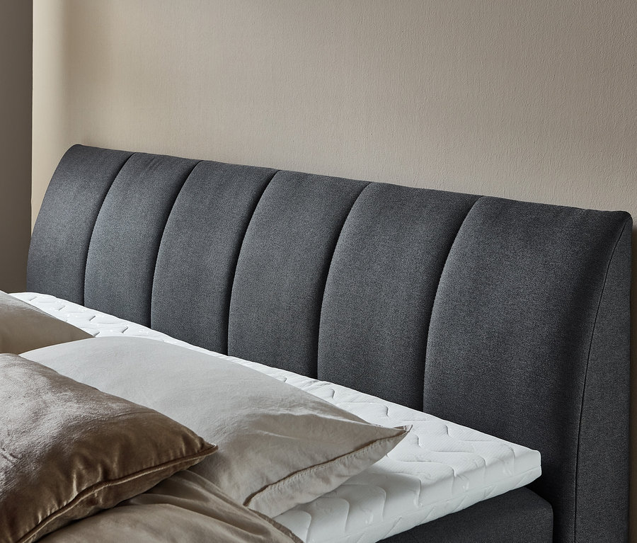Detailansicht eines grauen Polsterbetts mit Kissen und weißem Topper. DOMO collection Boxspringbett 180 x 200 cm inkl. Topper, groß