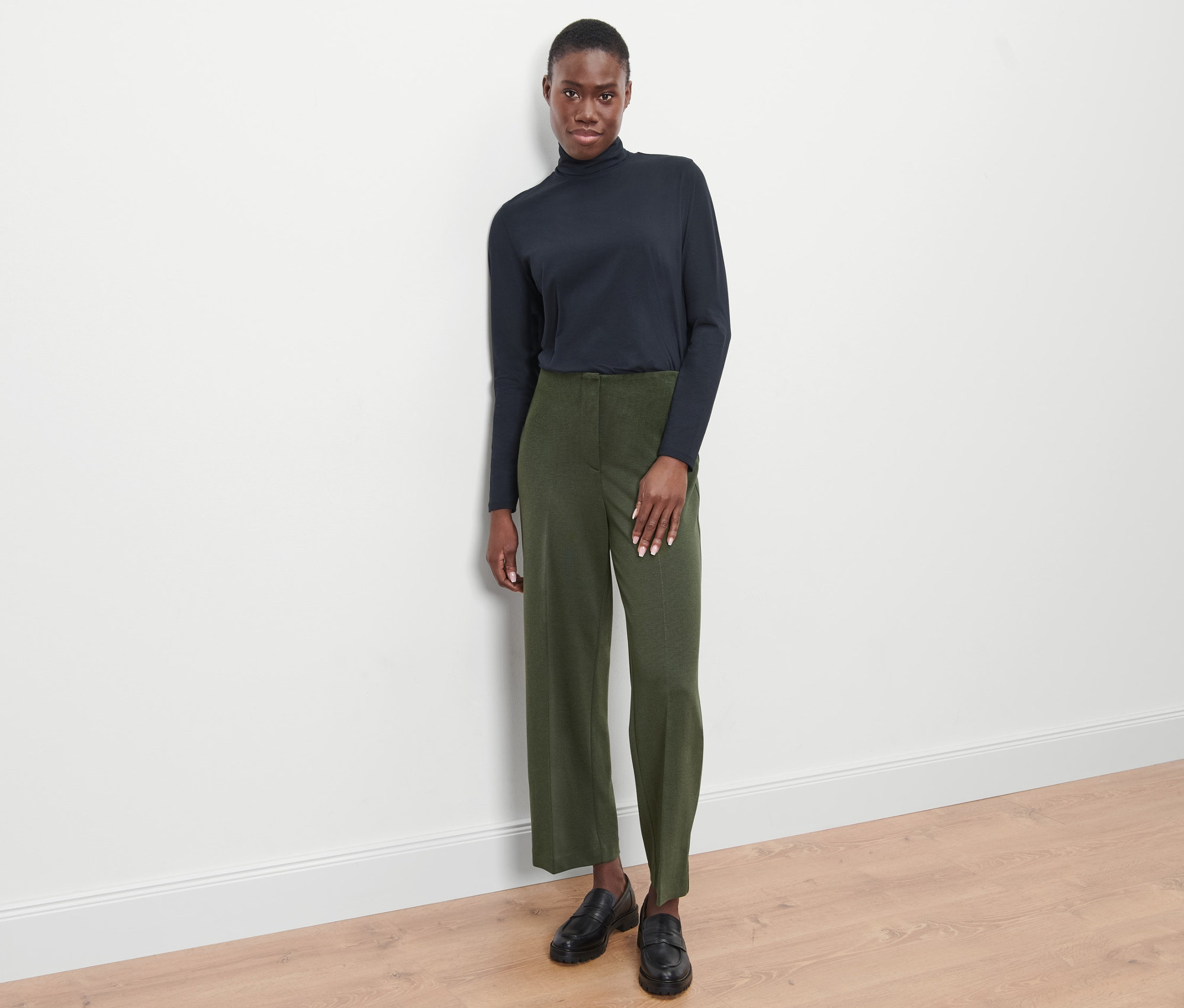 Frau steht und trägt eine Jerseyhose, grün meliert, und schwarze Schuhe.