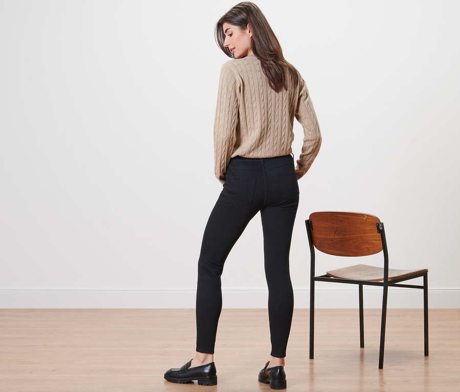 Eine Frau steht mit dem Rücken zur Kamera und trägt einen beigen Pullover und Jeggings.