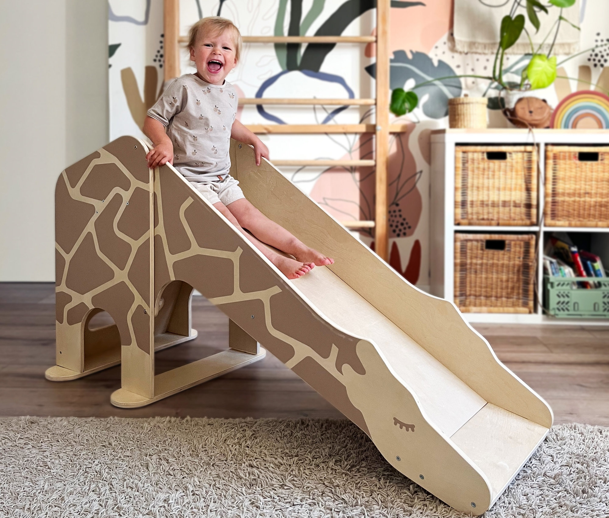 Ein Kind lacht und rutscht auf der small foot Indoor Rutsche Giraffe »Wildlife«.