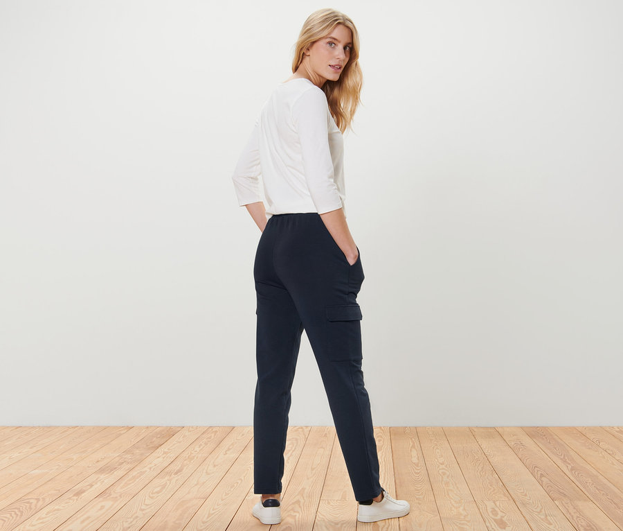 Eine Frau posiert in dunkelblauen Joggpants mit Cargo-Taschen und einem weißen Oberteil.