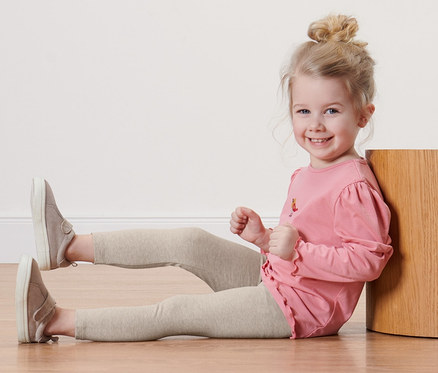 Lächelndes Mädchen sitzt mit einfarbigen Kinder-Leggings auf dem Boden.