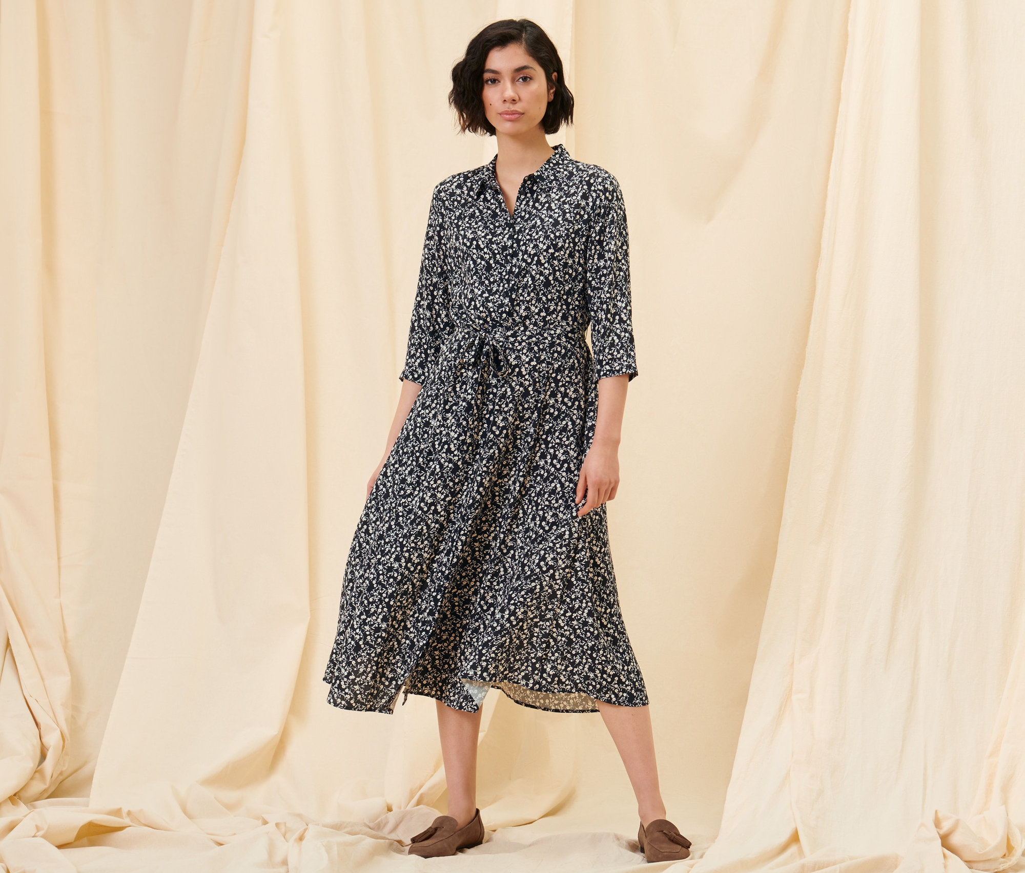Frau posiert in einem floralen Hemdblusenkleid und Loafern aus Veloursleder.