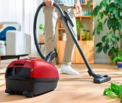 Mann saugt den Boden mit einem rot-schwarzen Bosch Bodenstaubsauger »BGD38RD1H« mit Beutel.