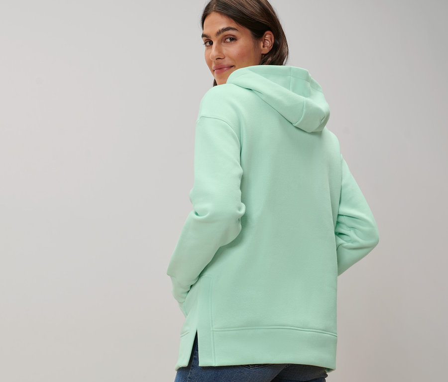 Frau blickt über die Schulter und trägt ein langes Kapuzensweatshirt.