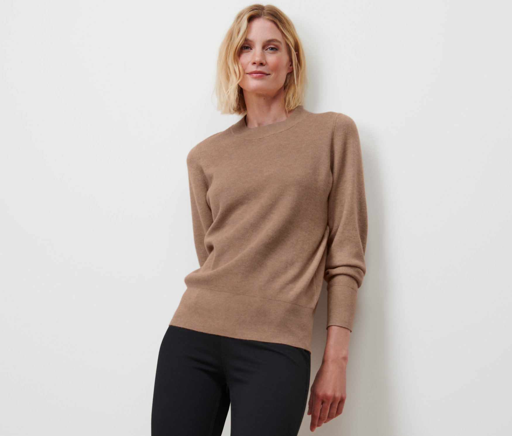 Frau posiert in Strickpullover und schwarzen Hosen.