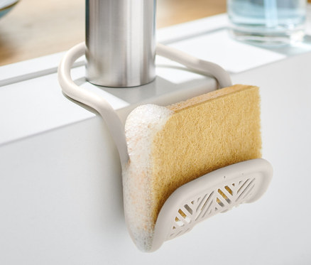 Schwammhalter mit Schwamm an einem Wasserhahn in einem weißen Waschbecken befestigt.