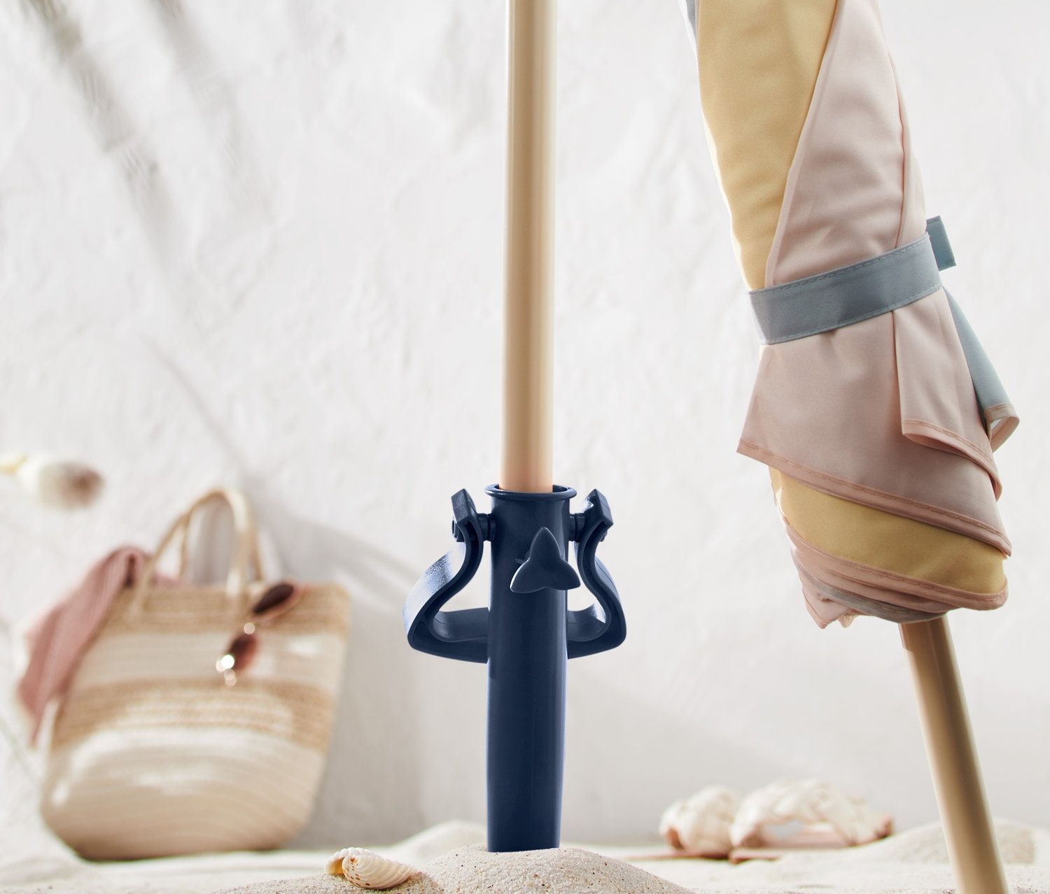 Ein pastellfarbener Sonnenschirm ist in einem blauen Schraub-Sonnenschirmhalter im Sand befestigt.