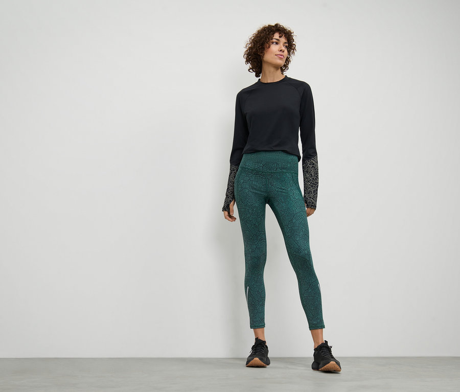 Eine Frau steht und trägt eine Sporttight und ein schwarzes Langarmshirt.