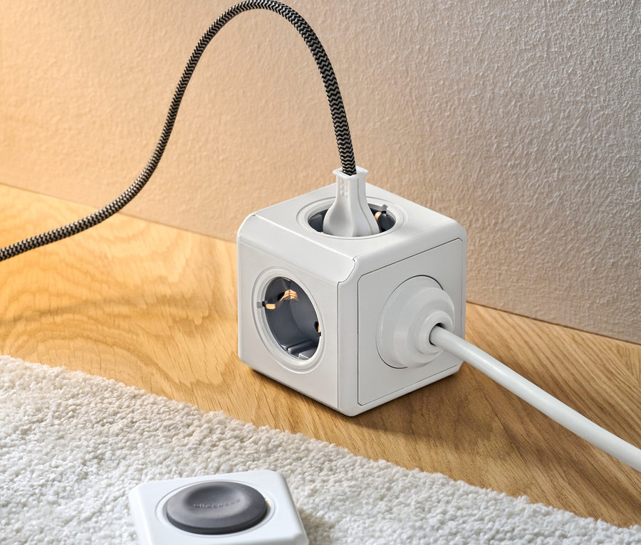 Weißer Steckdosenwürfel mit Fernbedienung auf Holzboden neben einem weißen Teppich.