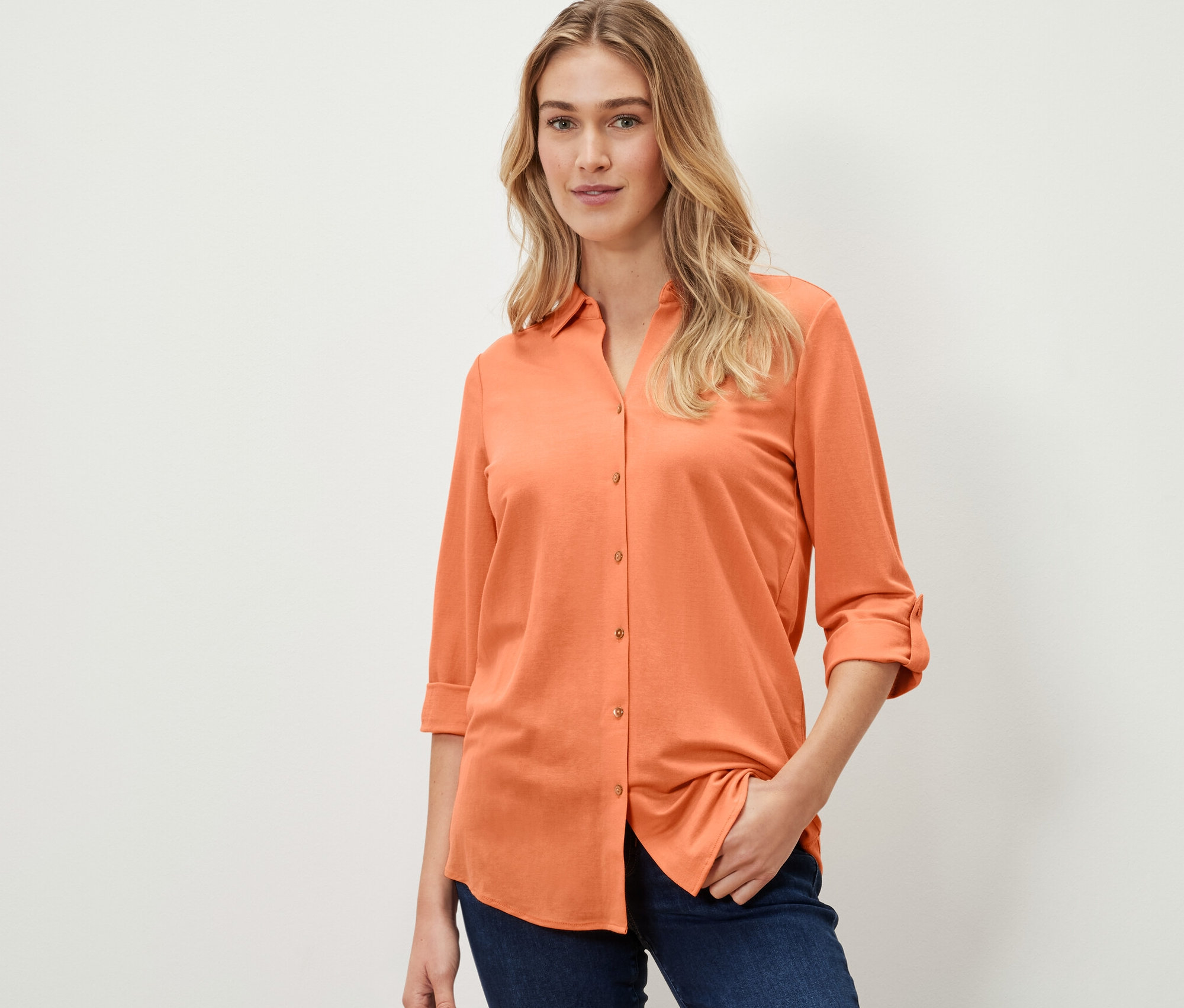 Frau trägt eine Piqué-Jerseybluse in Peach und Jeans.