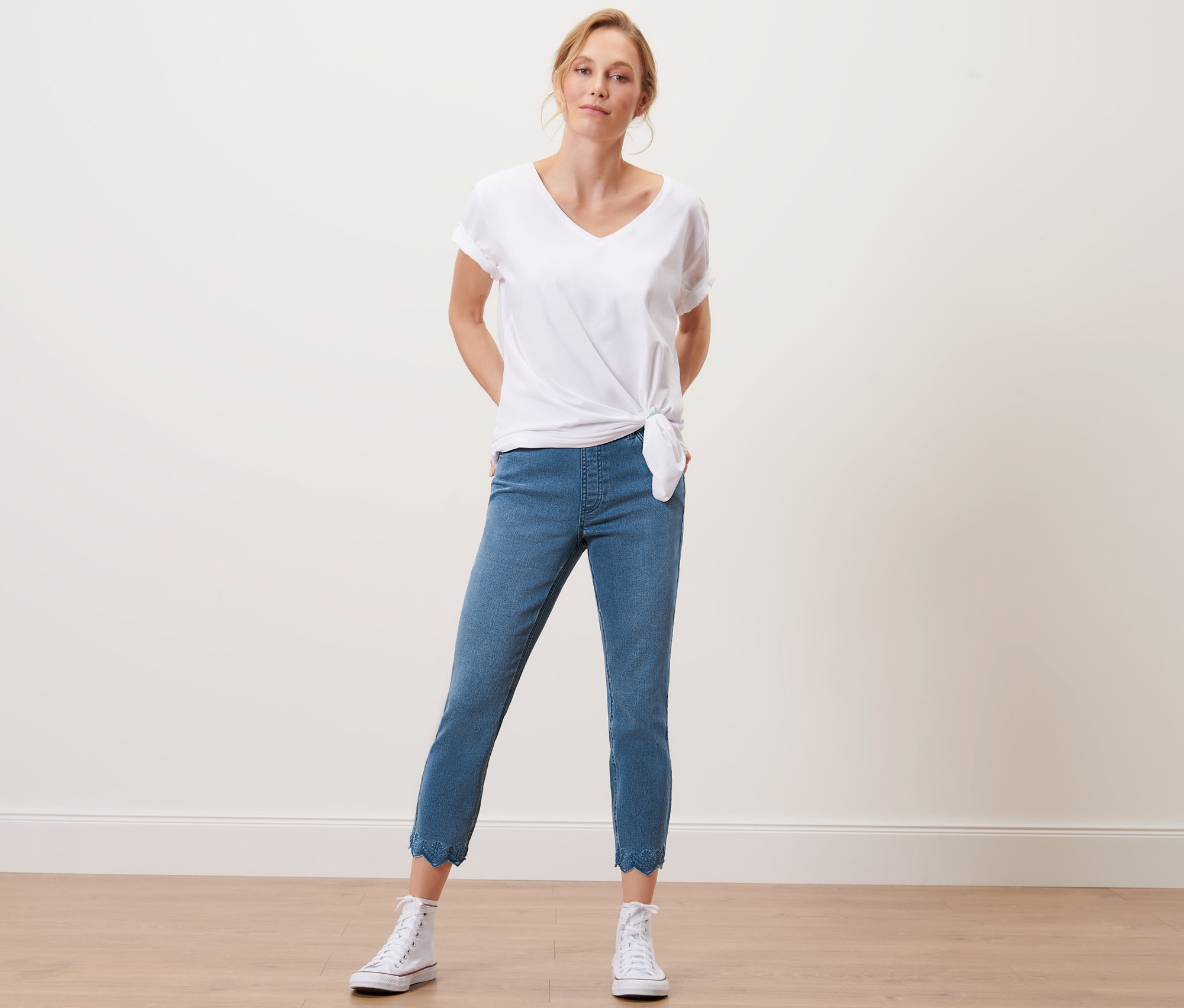 Frau posiert im Studio mit einem weißen T-Shirt und einer 7/8-Treggings mit Lochstickerei.