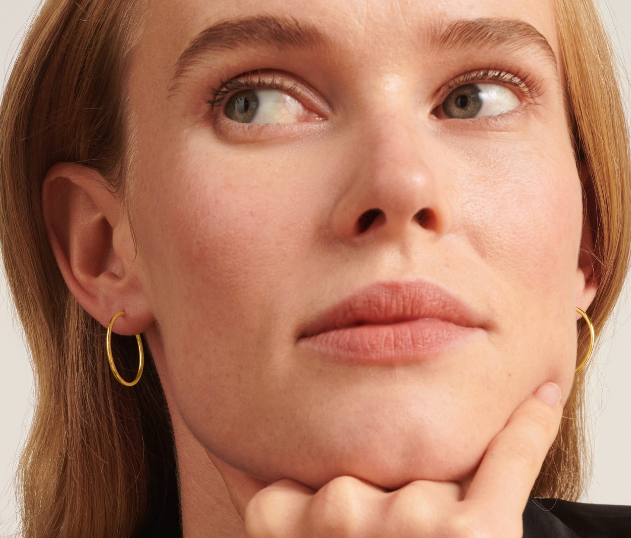 Frau mit flexiblen 585 Goldcreolen im Ohr, die nach oben schaut und ihr Kinn hält.